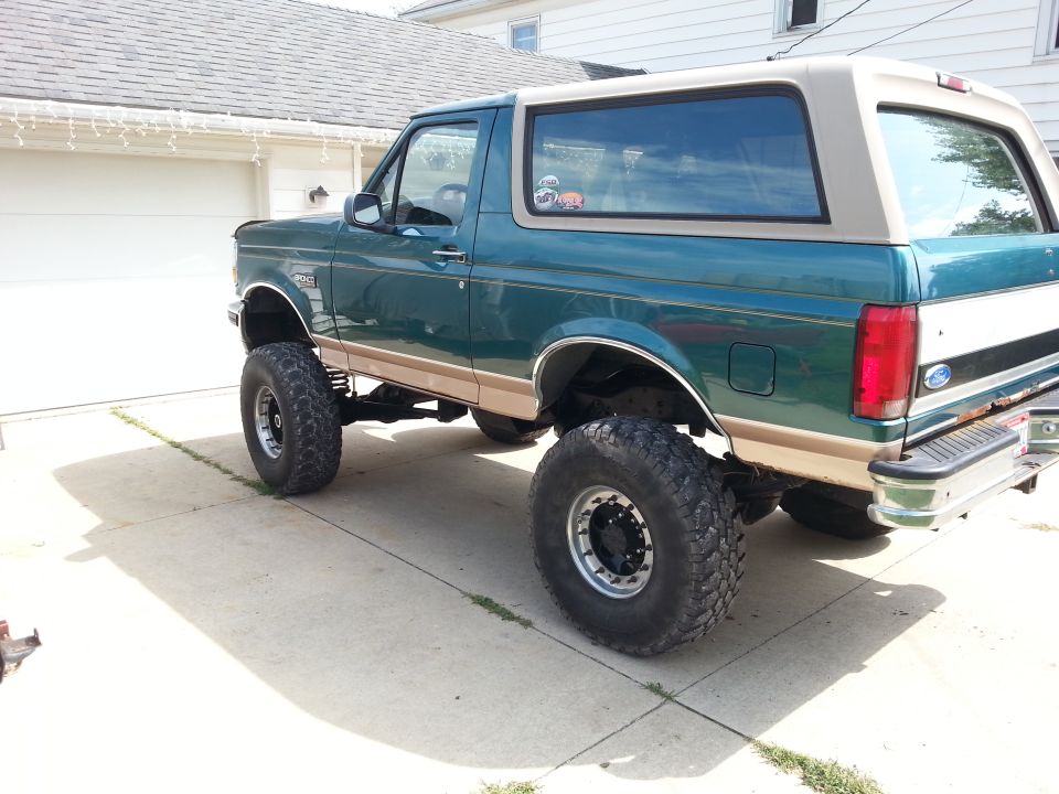 Green Ford Bronco with tan top, lifted with large tires, parked in a driveway