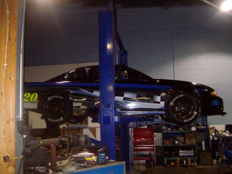 2004 Ford Crown Victoria - Race car with checkered flag graphics is raised on a shop lift, showing its side profile.