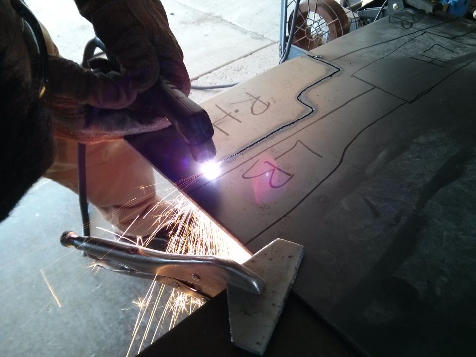 Metal sheet with drawn lines and 'RH' and 'LR' markings being cut by a plasma torch, sparks flying