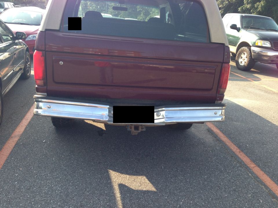 Rear of maroon Ford Bronco with tan top, parked next to other vehicles