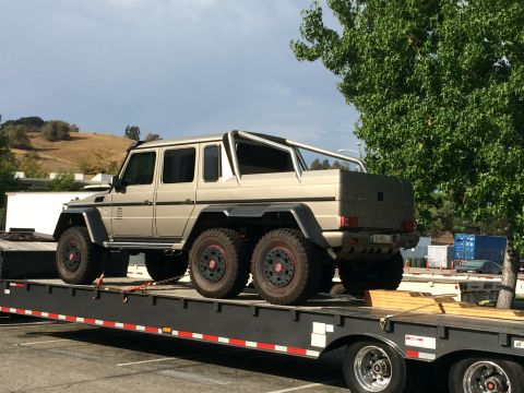 1968 Ford Mustang - A six-wheeled Mercedes-Benz G63 AMG 6x6 pickup truck is transported on a flatbed trailer under a partly cloudy sky.