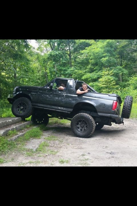 1995 Ford Bronco - This modified Ford Bronco is navigating an off-road trail with two occupants visible.