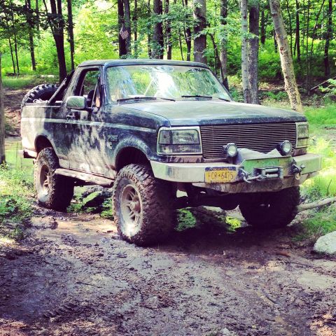 1995 Ford Bronco - This muddy Ford Bronco navigates a wooded trail, showing off its off-road modifications.