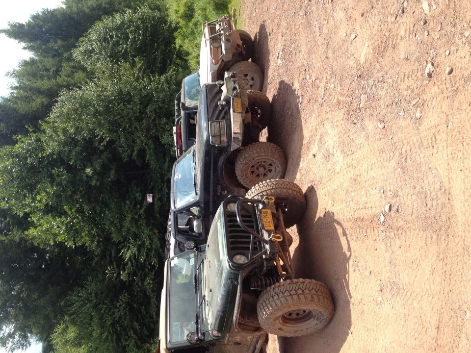 Several off-road vehicles parked in a line on a dirt path, with trees in the background