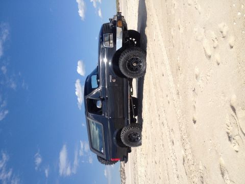 1995 Ford Bronco - A black 1995 Ford Bronco is parked on a sandy beach, with the ocean and sky in the background.