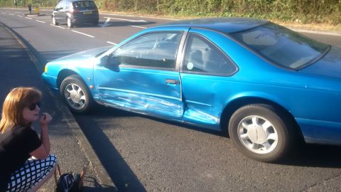 1994 Ford Thunderbird - A blue 1994 Ford Thunderbird coupe sits on the side of the road with extensive damage to its passenger side.