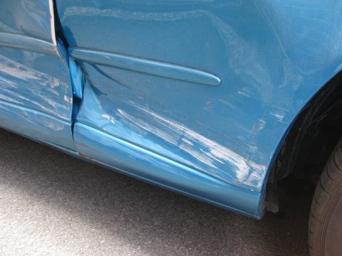 1994 Ford Thunderbird - The side panel of a blue vehicle shows extensive damage, including deep scratches and a noticeable dent.
