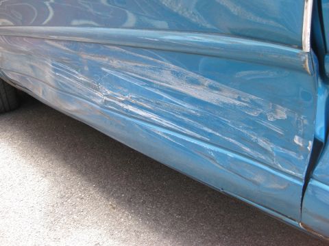 1994 Ford Thunderbird - This blue car door shows extensive damage from an accident, with deep scratches and dents marring the paintwork.