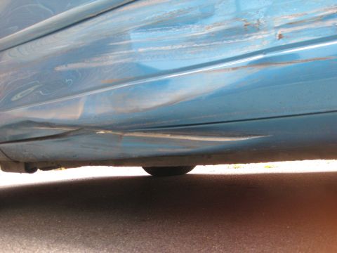 1994 Ford Thunderbird - Damage to the bottom of a car door, with visible dents and scraped paint.