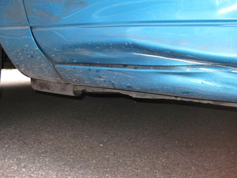 Close-up of a blue car's lower door panel showing significant damage and a detached rocker panel