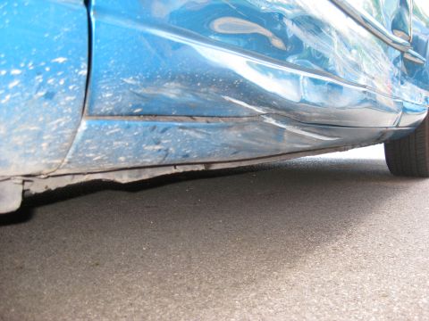 1994 Ford Thunderbird - The side panel of a blue car shows extensive damage, particularly along the lower section near the rocker panel.
