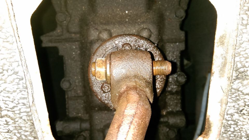 Rusty linkage arm bolted to cast housing with brass nut, seen through opening in panel