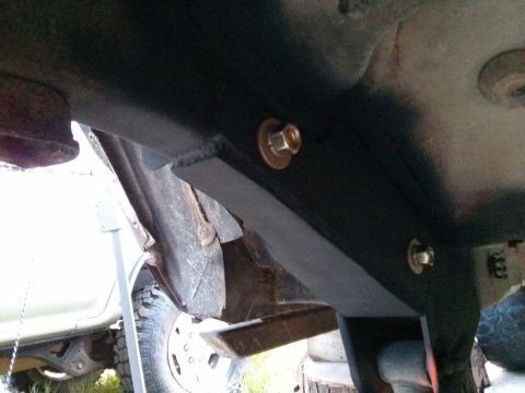 1986 Ford Bronco - Close-up view of a black metal bracket and bolts on the undercarriage of a vehicle, with a tire visible.