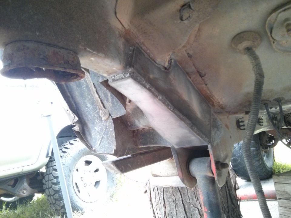 Close-up of rusty frame and suspension components under a vehicle, with a tire visible