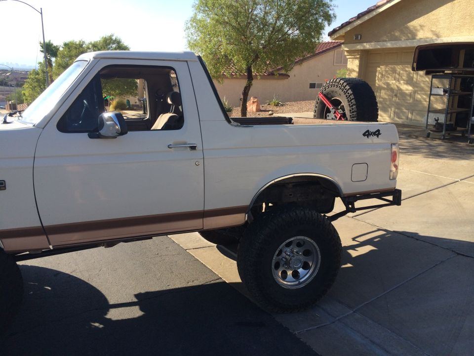 White Ford Bronco, lifted, with a spare tire in the bed. Side view