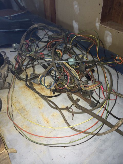 1964 Ford Fairlane - A pile of old automotive wiring is spread out on a dusty concrete floor, with a dark vehicle body visible in the background.