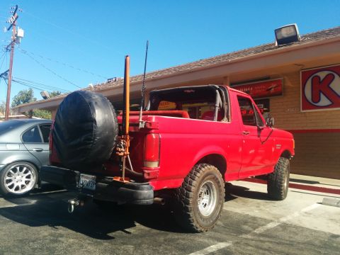 1988 Ford Bronco - This red 1988 Ford Bronco is seen from the rear, equipped with a spare tire and a fishing rod mounted on the back.