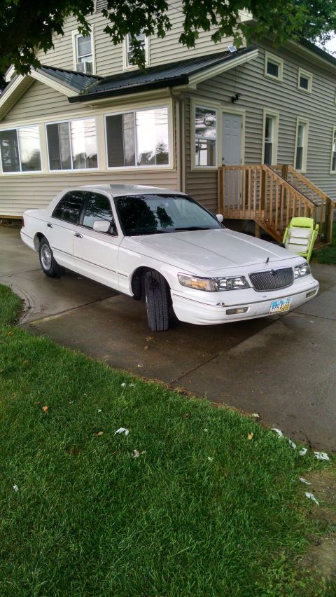 1997 Mercury Grand Marquis - A white 1997 Mercury Grand Marquis is parked in front of a house, showing its front quarter profile.