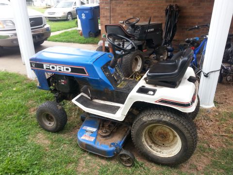 2002 Ford Expedition - A blue and white Ford riding mower is parked outdoors next to another mower and a bicycle.