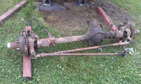 1990 Ford Bronco - A disassembled front axle assembly, likely for an older truck or SUV, lies on the grass.