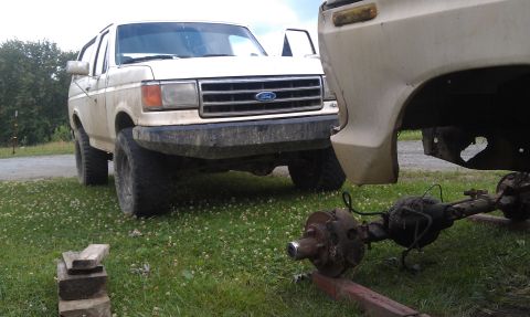 1990 Ford Bronco - A white 1990 Ford Bronco is seen from the front, parked on grass next to a removed axle assembly.