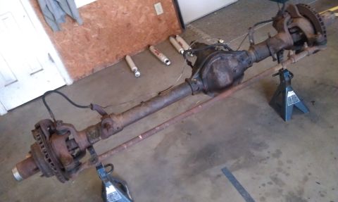 1990 Ford Bronco - A disassembled front axle assembly rests on jack stands in a garage setting.