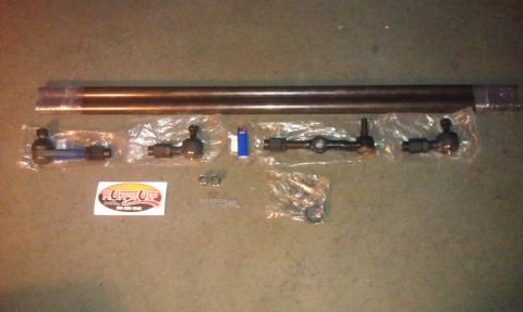 1990 Ford Bronco - Various steering linkage components are displayed on a textured surface, alongside a brand sticker and hardware.