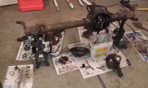 1990 Ford Bronco - A disassembled differential axle assembly is spread out on the floor, with various components and tools scattered on newspapers.