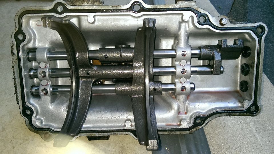 Transmission shift forks and shafts inside a metal casing with a black gasket
