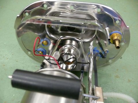 Underside view of a chrome fuel pump assembly with electrical connections and fuel line fittings