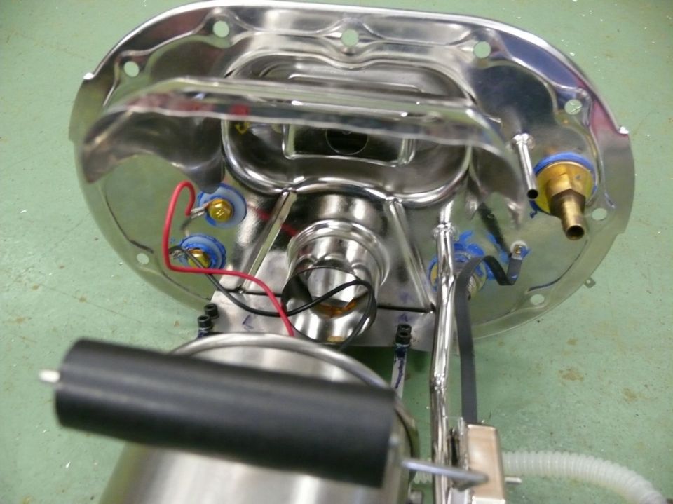 Underside view of a chrome fuel pump assembly with electrical connections and fuel line fittings