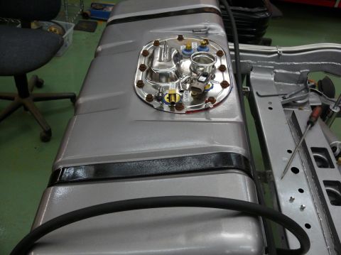 Silver fuel tank with chrome sending unit and black banding, mounted to a chassis