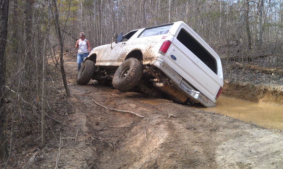 White 1990 Ford Bronco tilted on muddy off-road trail