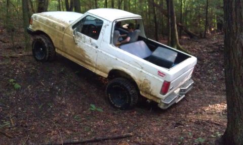 1990 Ford Bronco - A white Ford Bronco II navigates a muddy trail through a forest.