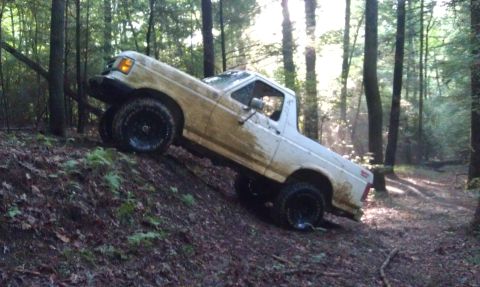 1990 Ford Bronco - A white pickup truck navigates a steep, wooded trail.