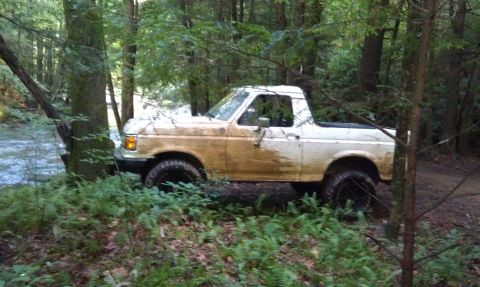 1990 Ford Bronco - Muddy 1990 Ford Bronco parked off-road in a forest setting.