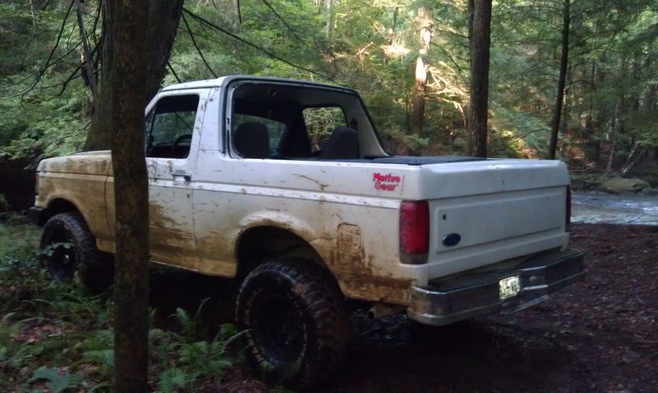 White Ford Bronco parked on a dirt path next to a stream in a forest