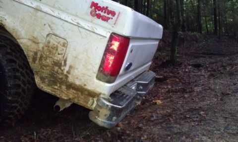 1990 Ford Bronco - Mud-covered white Ford Bronco seen from the rear in a wooded area.
