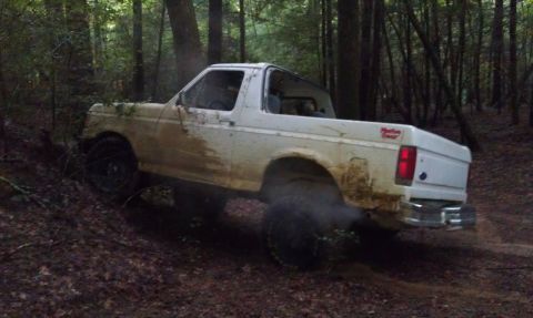 1990 Ford Bronco - White 1990 Ford Bronco navigating a muddy trail through a forest.