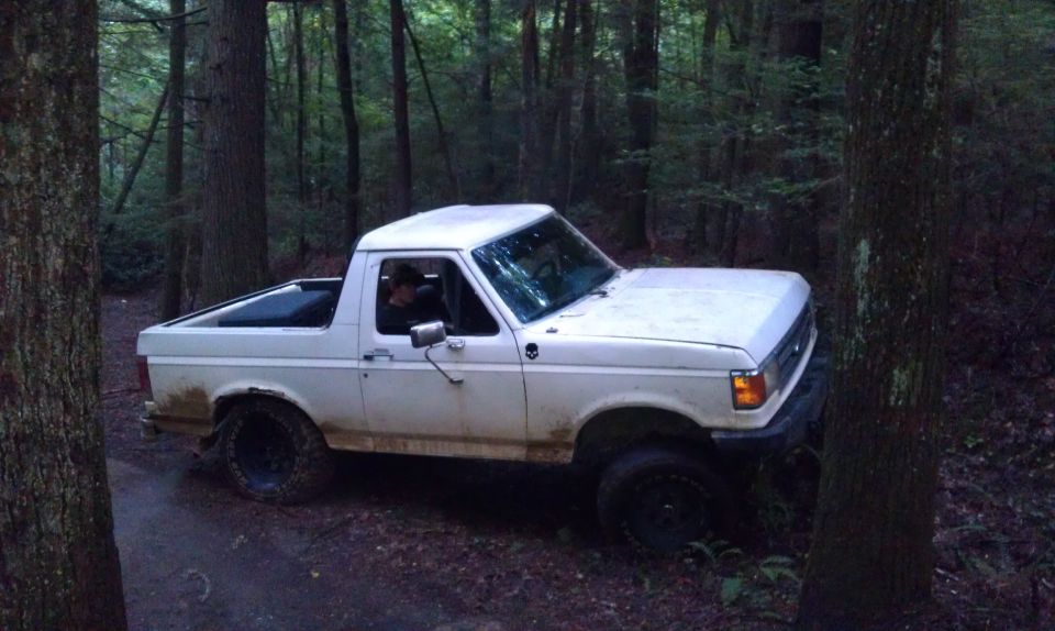 White Ford Bronco driving on a dirt path in a forest