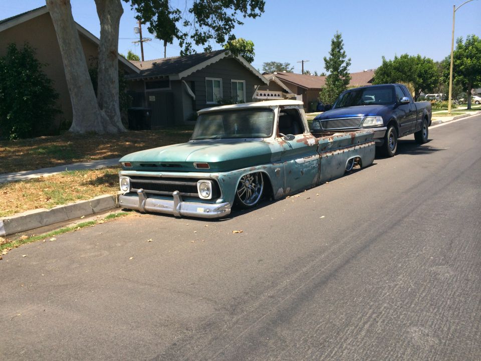 Teal and rust pickup truck with lowered suspension and chrome wheels parked on a residential street