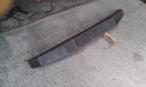 1990 Ford Bronco - A fabricated steel bumper sits on wooden blocks on a concrete surface, with an angle grinder in the background.