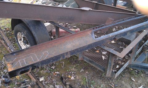 1990 Ford Bronco - A trailer frame with various metal beams and cutouts, showing chalk markings on one of the beams.