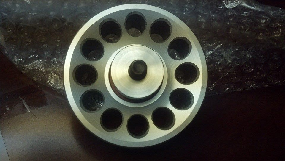 Drilled aluminum pulley with raised center hub on a dark surface over bubble wrap