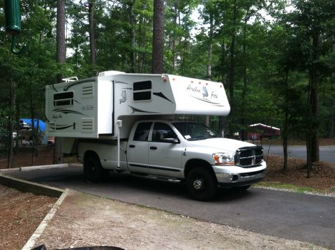 2006 Dodge 3500 - White 2006 Dodge 3500 pickup truck equipped with an Arctic Fox camper shell is parked in a campsite.