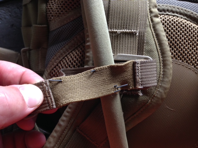 Tan fabric strap on a backpack, held by a hand, with metal staples visible