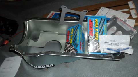 1972 Ford Ranchero - A collection of engine parts including an oil pan, bolts, studs, and gaskets are laid out on a surface.