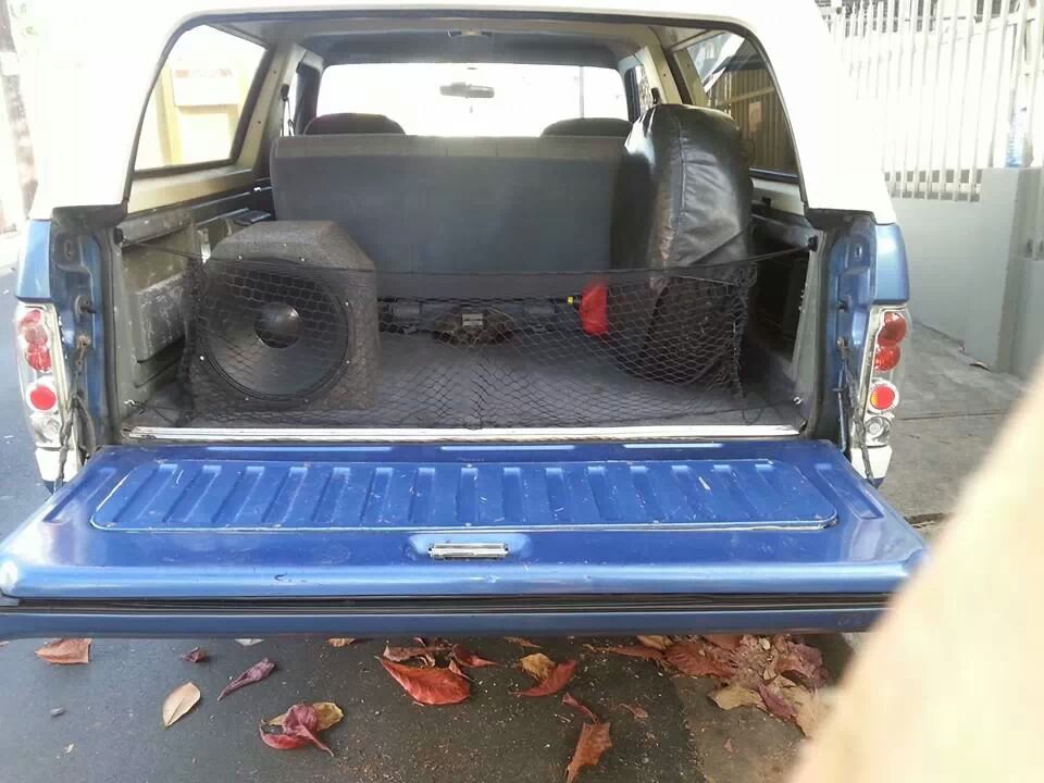 Back of a blue and white SUV with a large subwoofer and spare tire in the cargo area