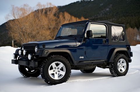 2000 Jeep Wrangler - A dark blue 2000 Jeep Wrangler is parked in a snowy landscape, aftermarket front lights and a soft top.