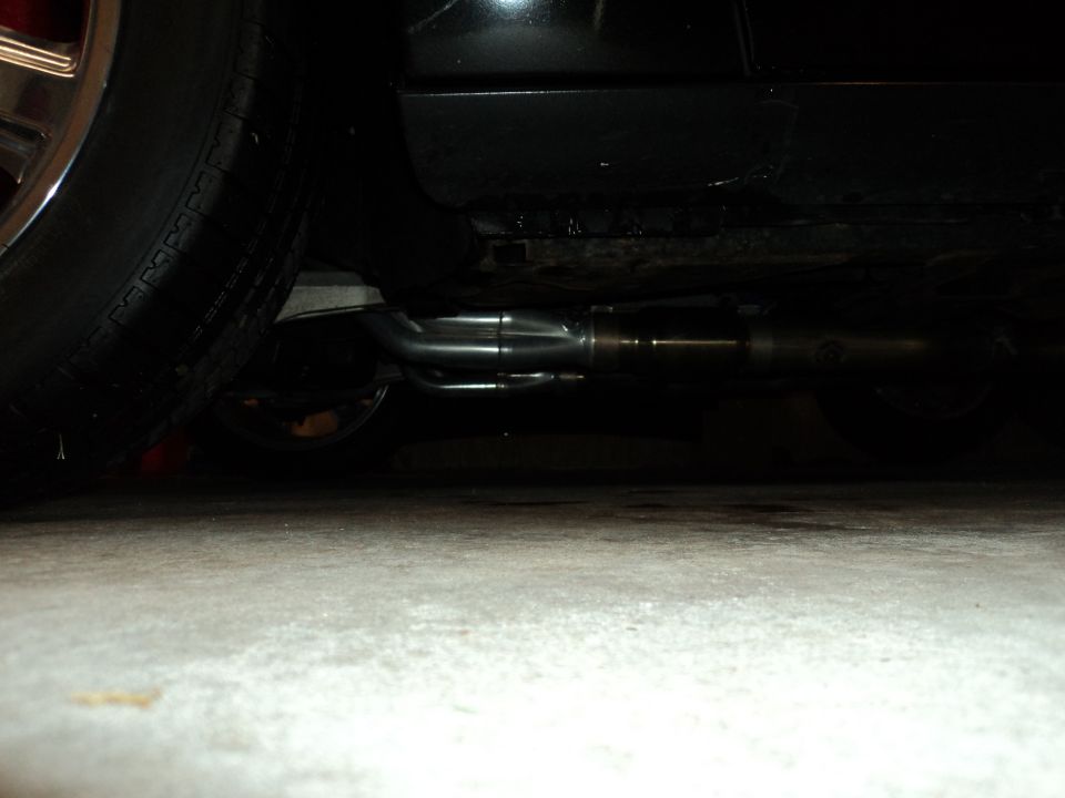 Black car exhaust system with dual pipes visible from underneath, near a tire